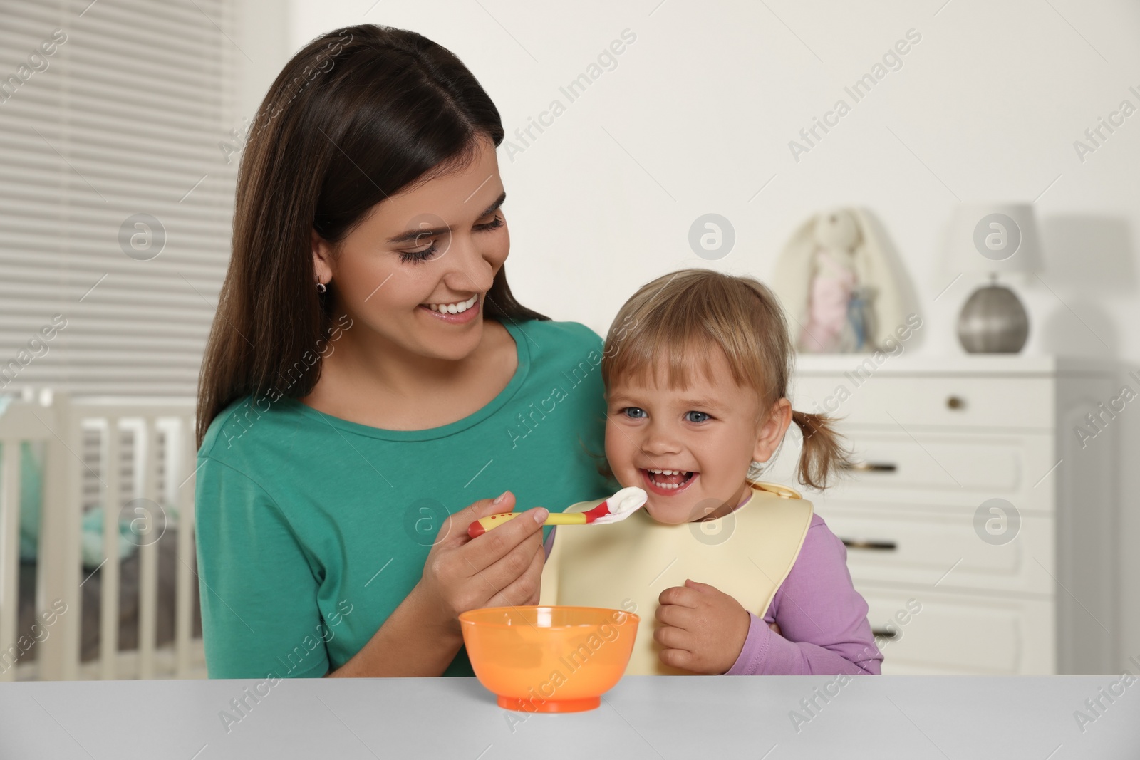 Photo of Mother feeding her cute little child with yogurt at white table in room