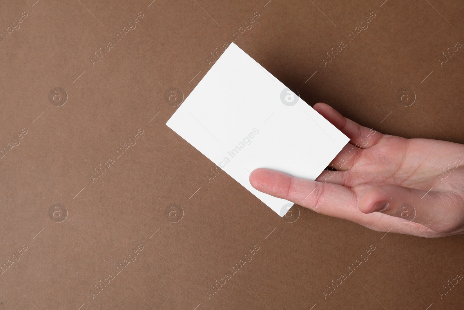 Photo of Man holding paper card on brown background, top view. Mockup for design