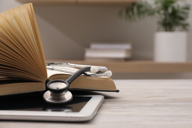 Photo of Book, tablet and stethoscope on wooden table indoors, closeup with space for text. Medical education