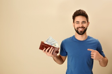 Photo of Happy young man with wallet full of money on color background. Space for text