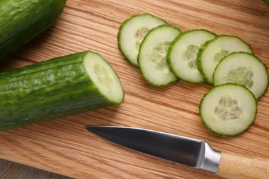 Photo of Cut cucumber and knife on wooden board, top view