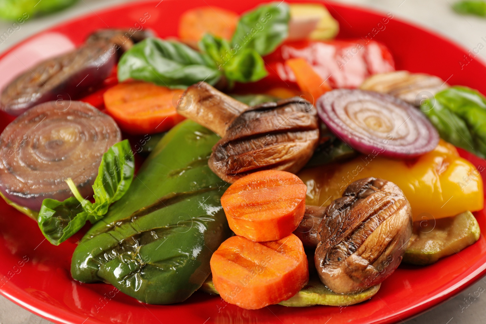 Photo of Delicious grilled vegetables with basil on red plate, closeup