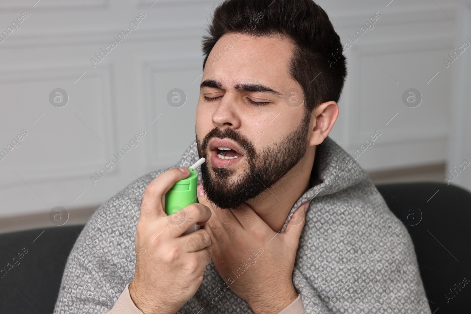 Photo of Young man using throat spray at home