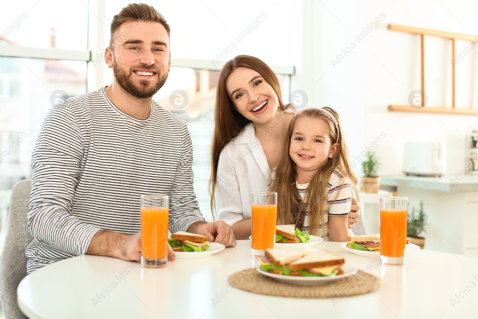 Photo of Happy family having breakfast with sandwiches at table in kitchen