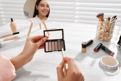 Photo of Woman with eyeshadow palette and brush at dressing table indoors, closeup