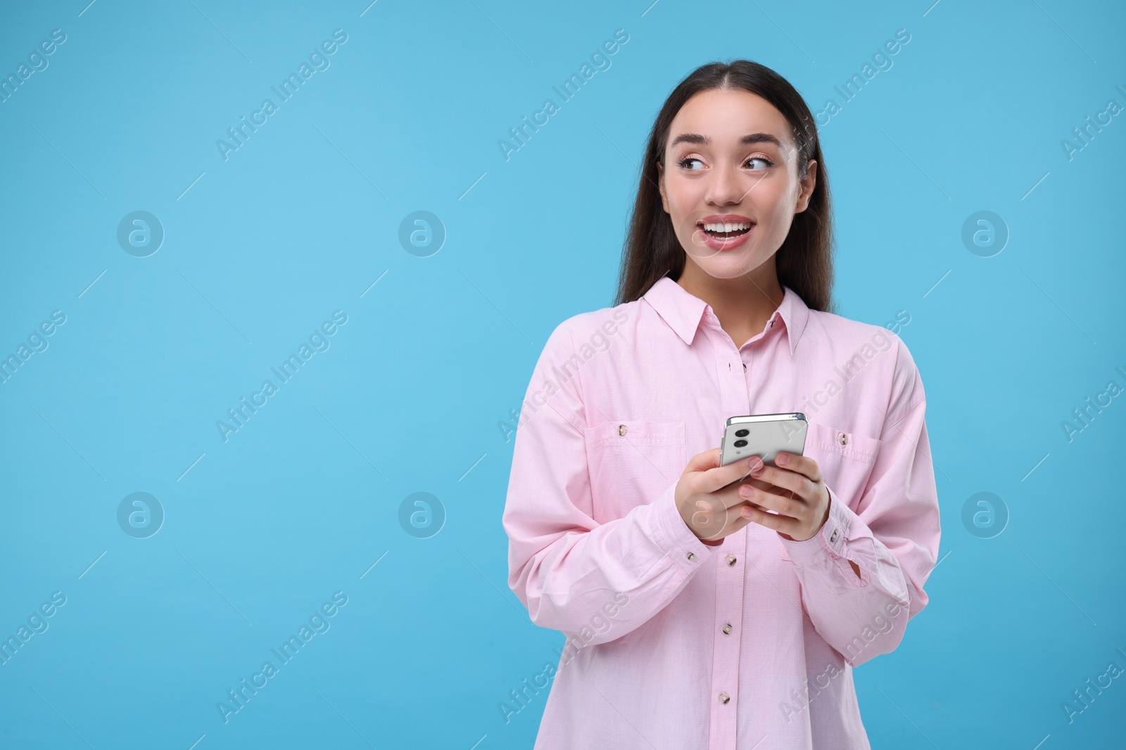 Photo of Happy woman sending message via smartphone on light blue background, space for text