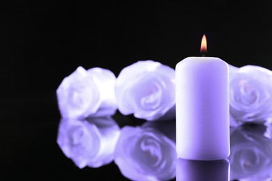 Image of Violet roses and burning candle on black mirror surface, space for text. Funeral attributes