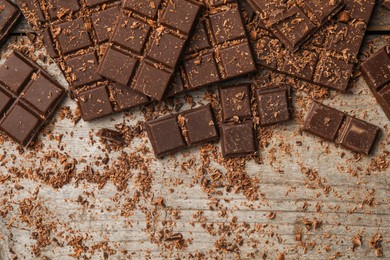 Pieces and shavings of tasty chocolate bars on wooden table, flat lay. Space for text