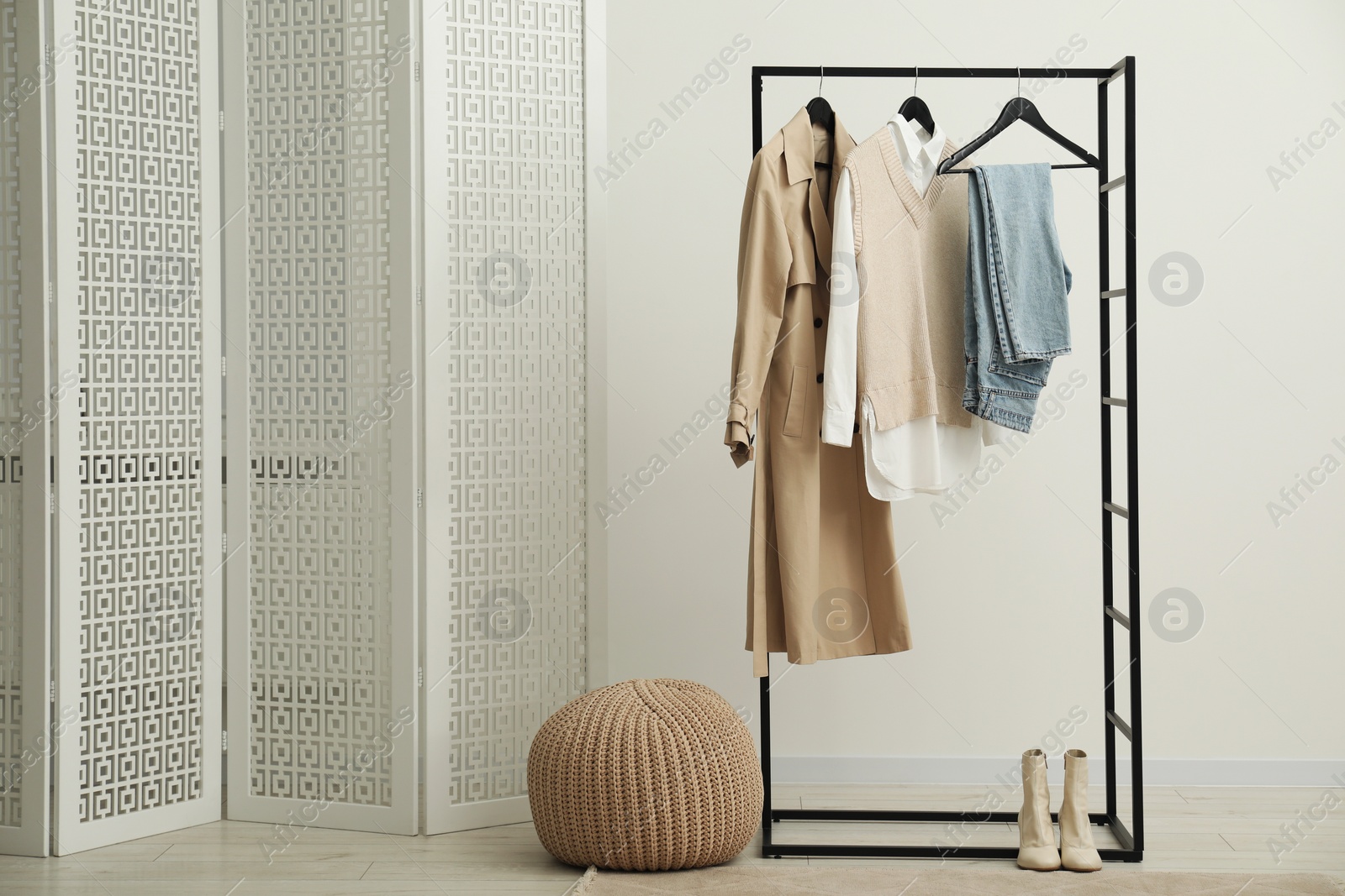 Photo of Rack with different stylish women's clothes, boots, pouf and folding screen indoors