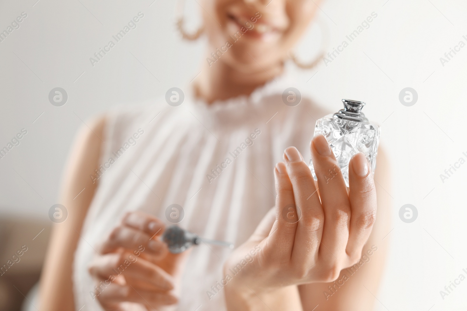 Photo of Young woman applying perfume on wrist against blurred background, closeup