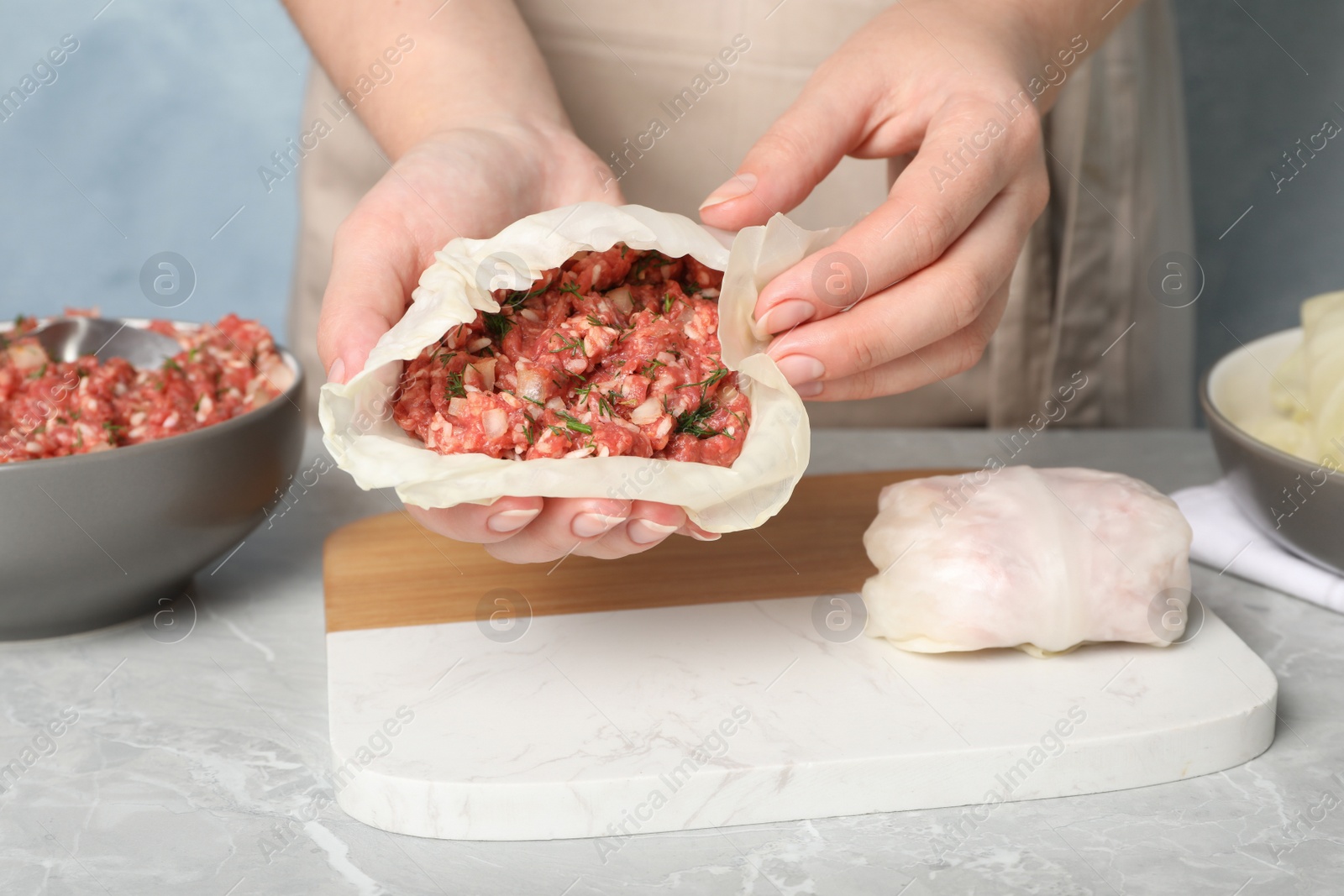 Photo of Woman preparing stuffed cabbage rolls at light grey table, closeup