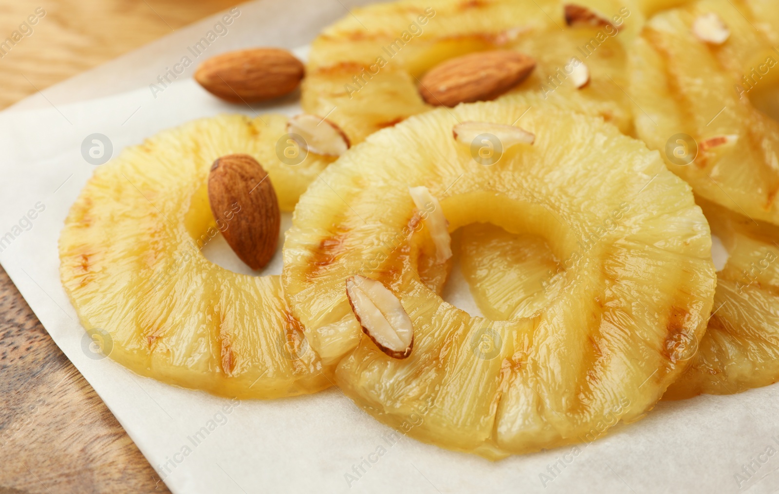 Photo of Tasty grilled pineapple slices and almonds on wooden table, closeup