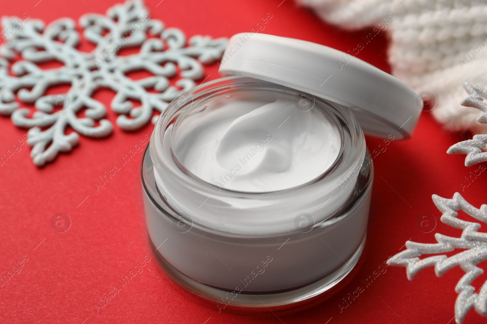 Photo of Winter skin care. Hand cream near decorative snowflakes on red background, closeup