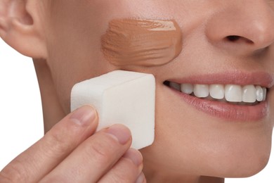 Woman blending foundation on face with makeup sponge against white background, closeup