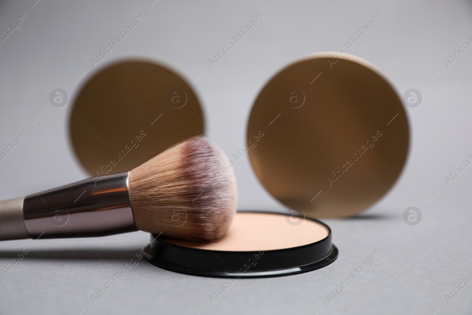 Photo of Open face powder and brush on light grey background, closeup