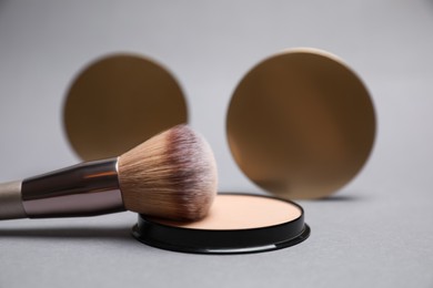 Photo of Open face powder and brush on light grey background, closeup