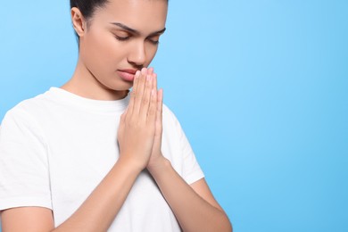 African American woman with clasped hands praying to God on light blue background. Space for text