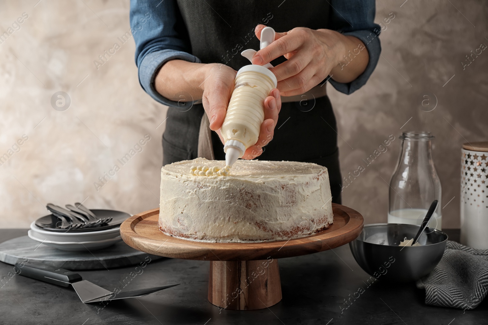 Photo of Woman decorating delicious cake with fresh cream at table indoors, closeup. Homemade pastry