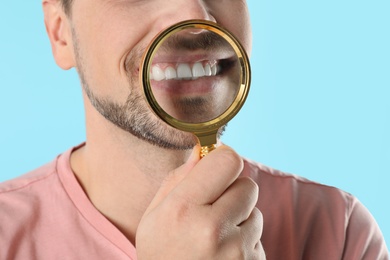 Photo of Smiling man with perfect teeth and magnifier on color background, closeup