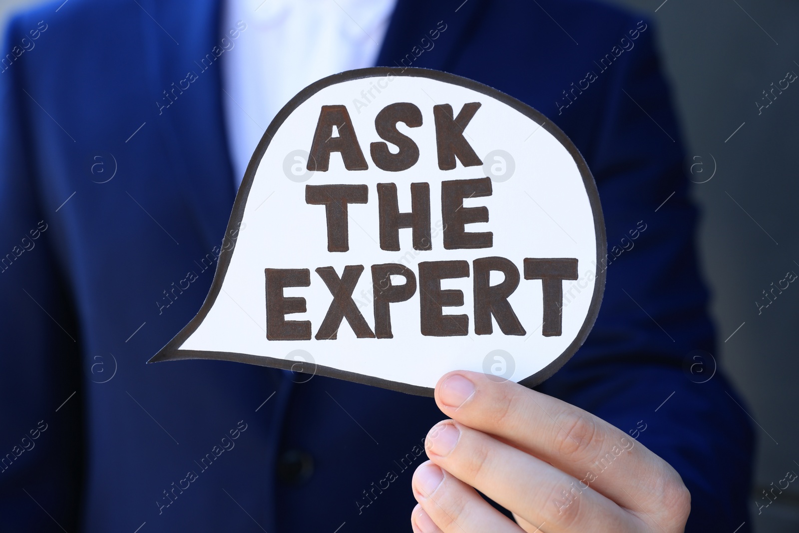 Photo of Man holding card with phrase Ask The Expert near black wall, closeup
