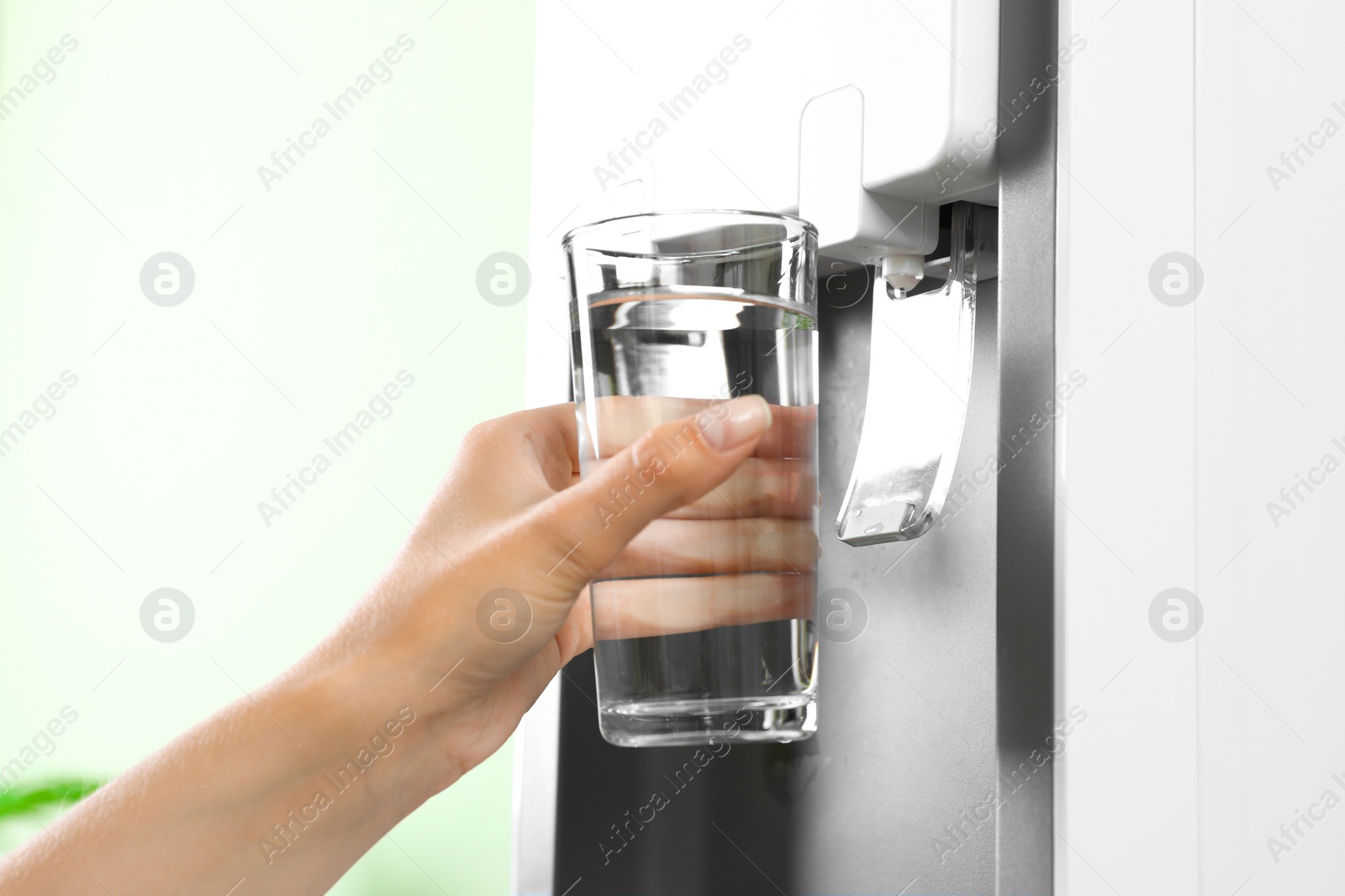 Photo of Woman filling glass from water cooler indoors, closeup. Refreshing drink