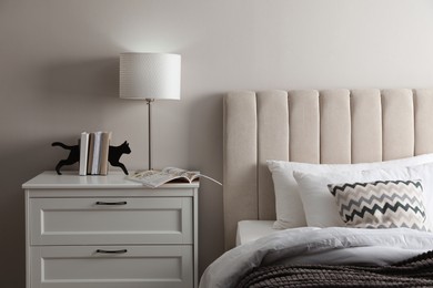 Photo of Stylish lamp, books and magazine on bedside table indoors. Bedroom interior elements