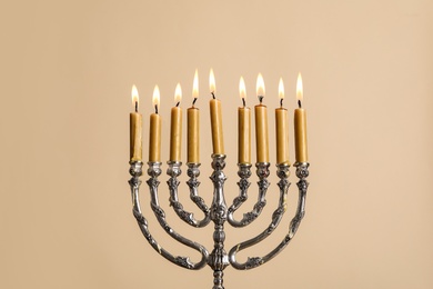 Photo of Silver menorah with burning candles on beige background. Hanukkah celebration