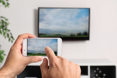 Photo of Woman with smartphone connected to TV set in living room
