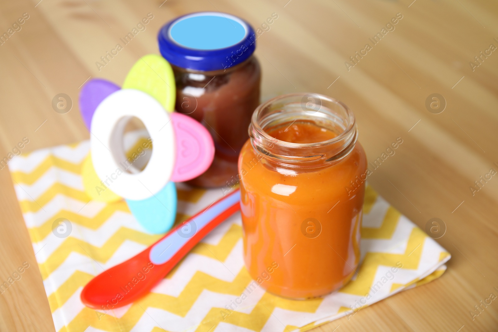 Photo of Jars with healthy baby food, spoon and toy on wooden table