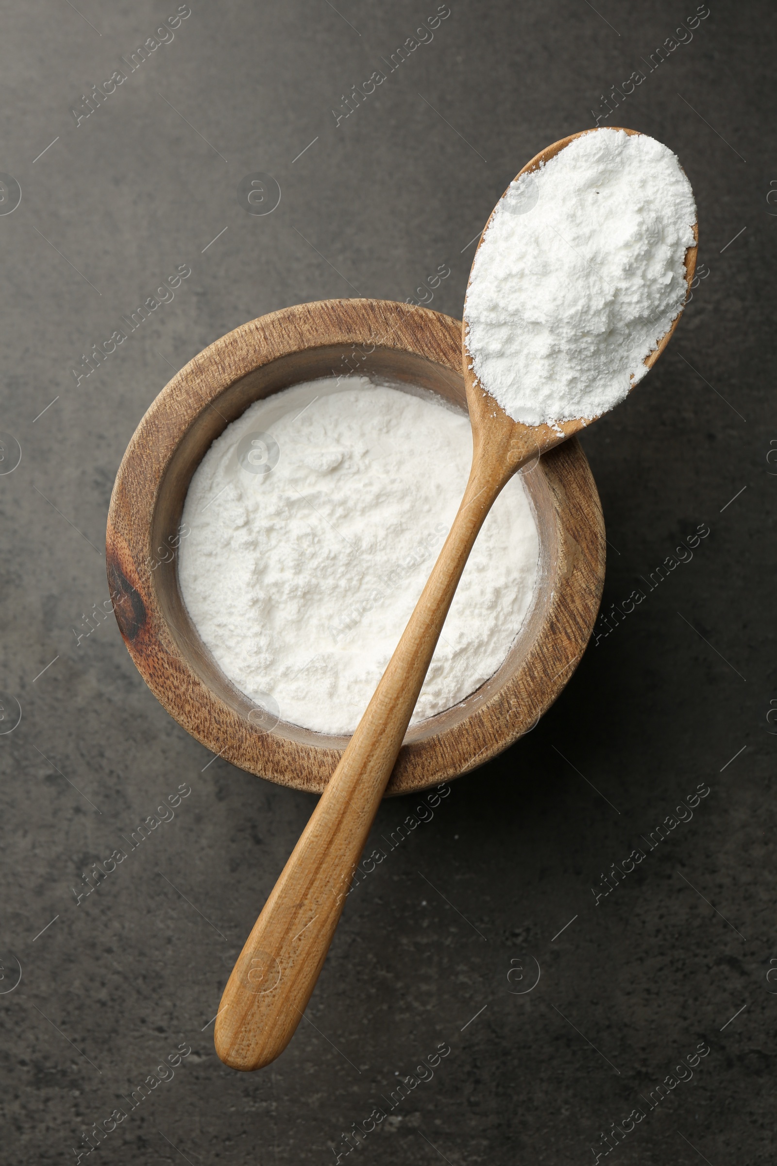 Photo of Baking powder in bowl and spoon on grey textured table, top view