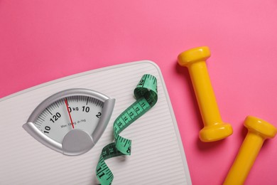 Weight loss concept. Scales, dumbbells and measuring tape on pink background, flat lay