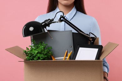 Unemployed woman holding box with personal office belongings on pink background, closeup
