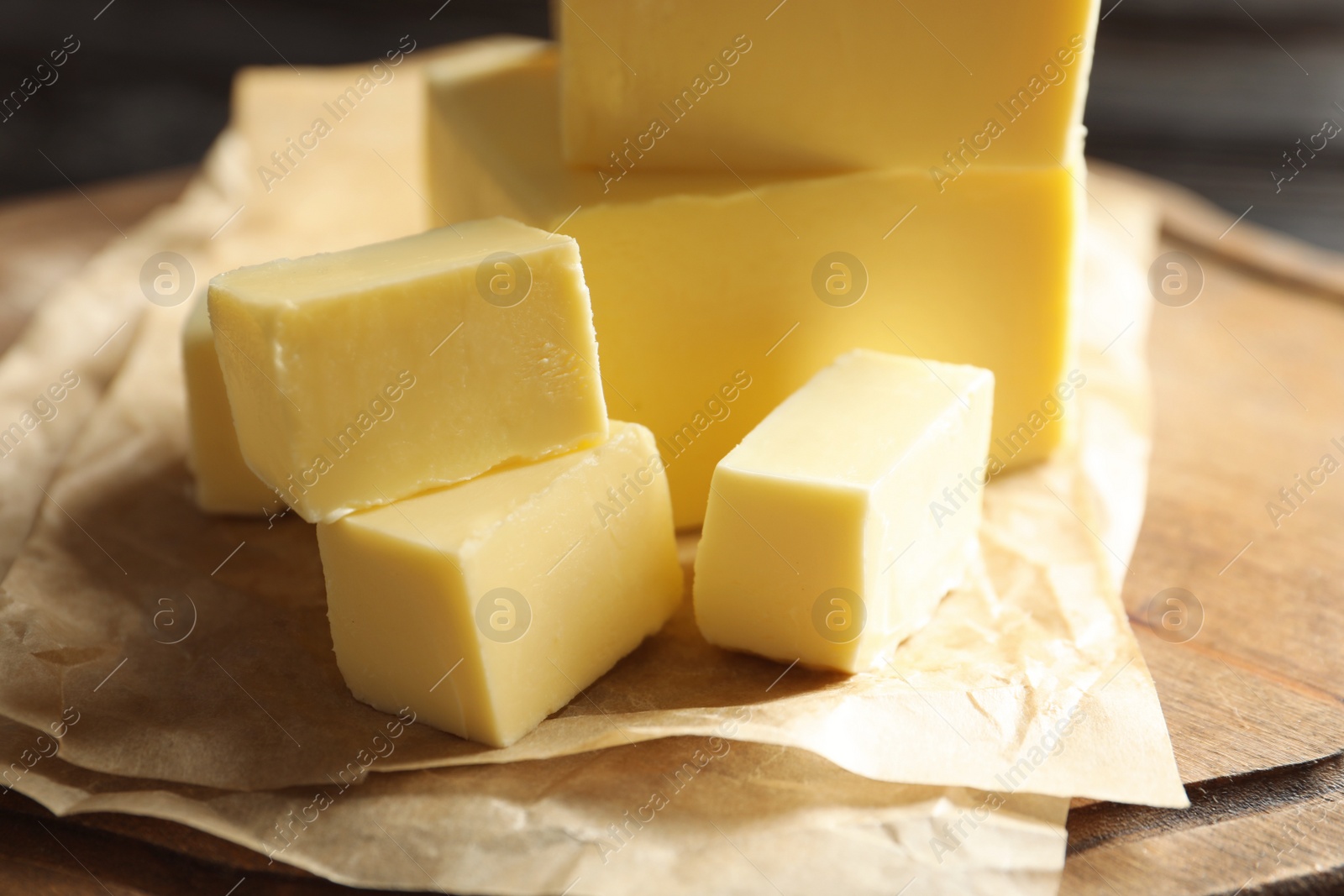 Photo of Fresh butter with parchment on wooden board, closeup