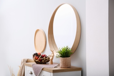 Photo of Round mirror and chest of drawers near grey wall in hallway. Interior design