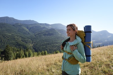 Tourist with backpack and sleeping pad in mountains on sunny day