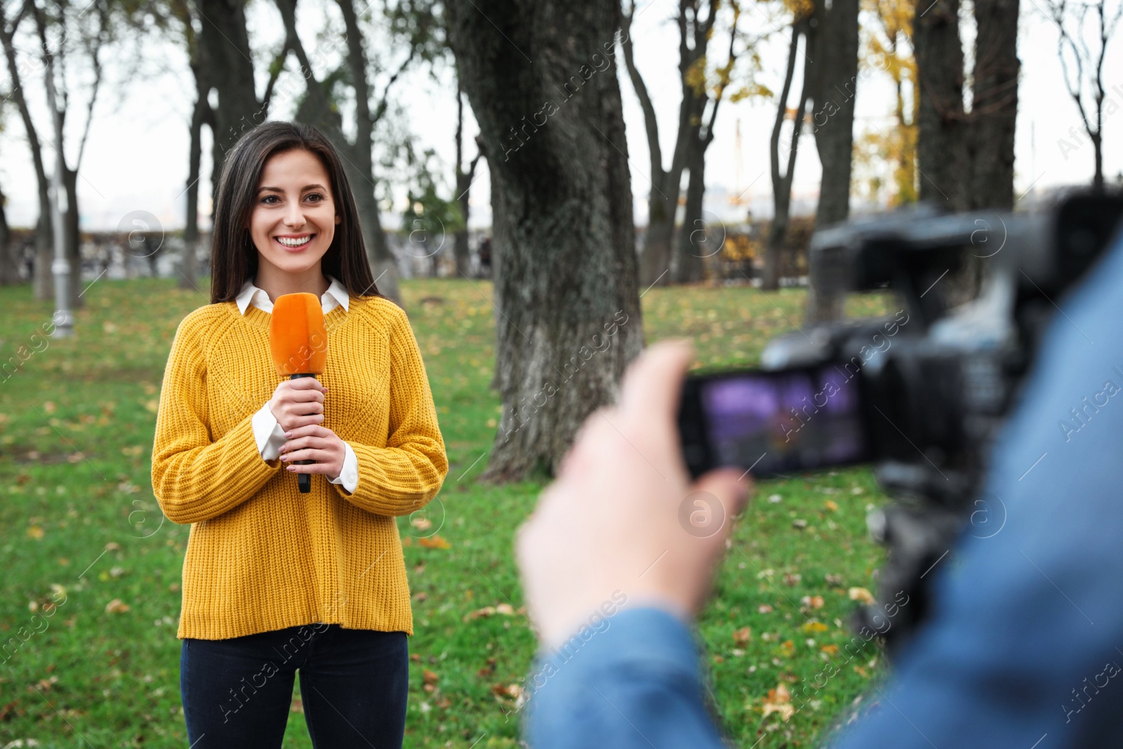 Photo of Young journalist and video operator working in park