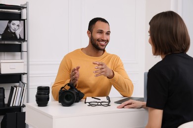 Young professional photographer with camera talking with woman in modern photo studio