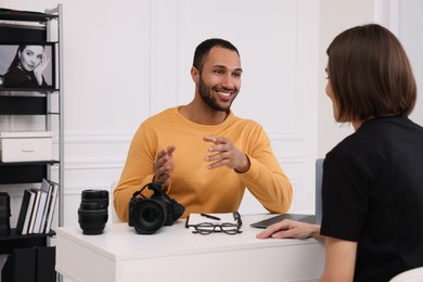 Photo of Young professional photographer with camera talking with woman in modern photo studio