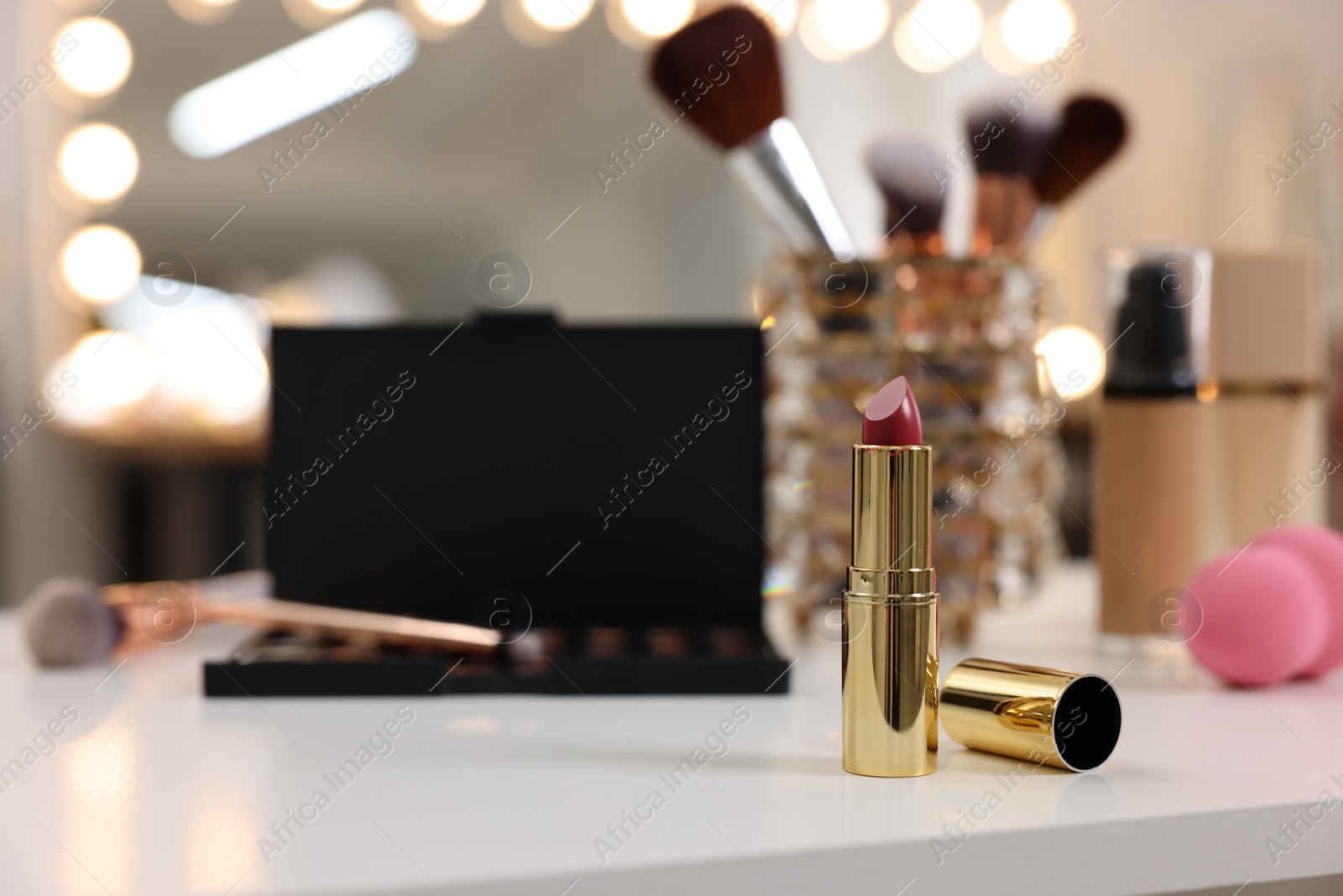 Photo of Red lipstick and other cosmetic products on white table in makeup room, selective focus