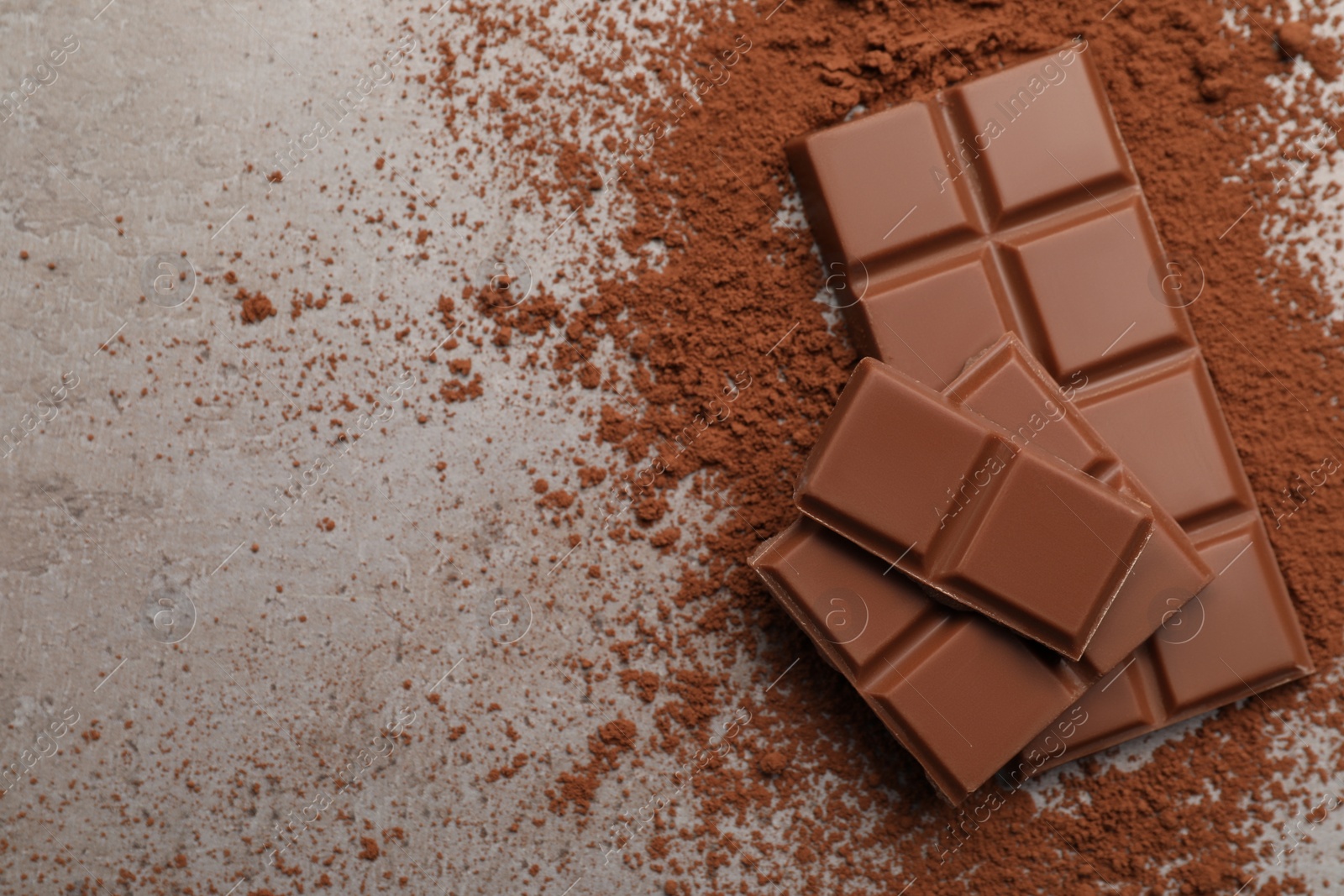 Photo of Delicious milk chocolate and cocoa powder on light grey table, flat lay. Space for text