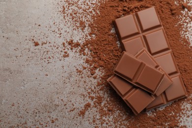 Delicious milk chocolate and cocoa powder on light grey table, flat lay. Space for text