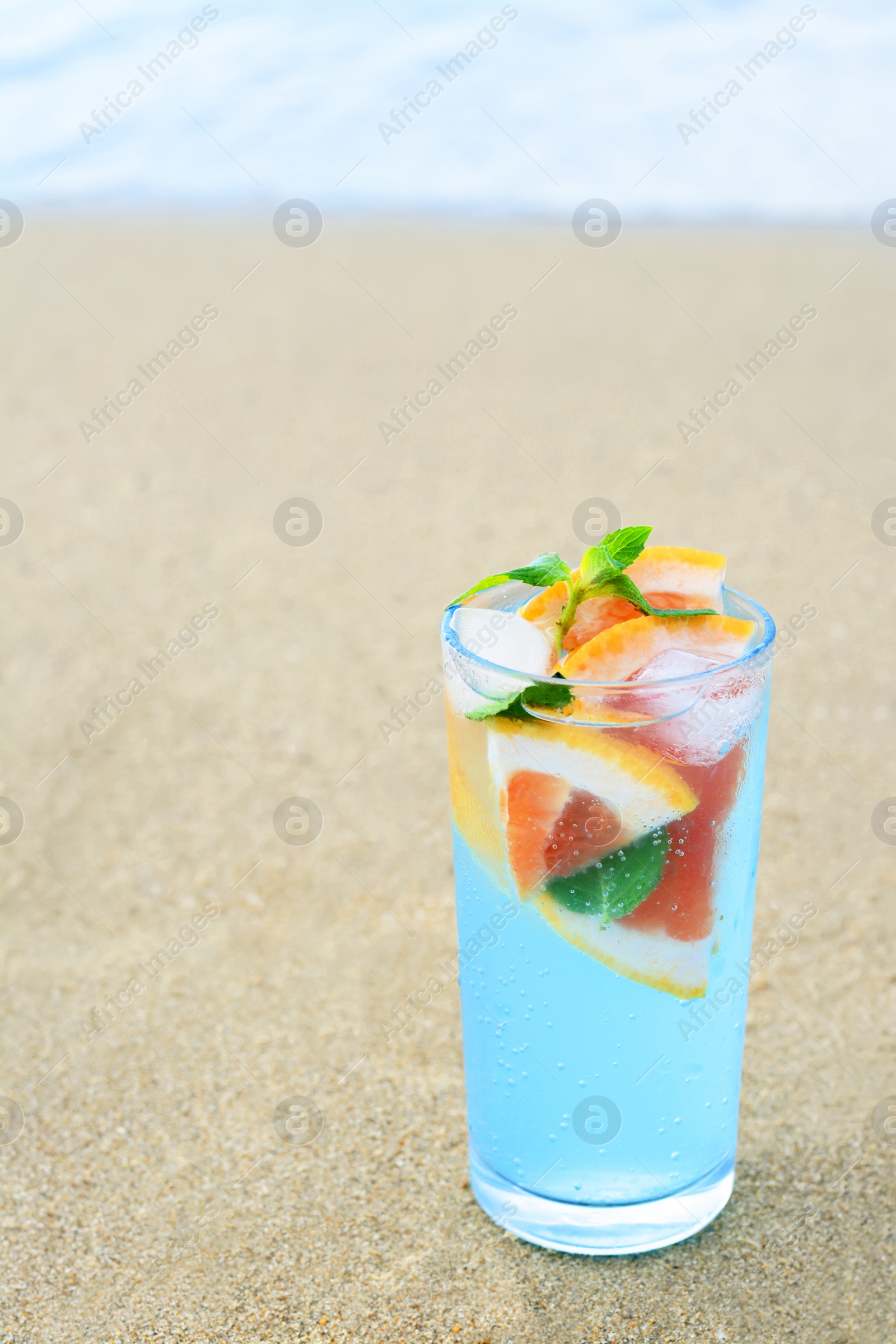 Photo of Glass of refreshing drink with grapefruit and mint on sandy beach