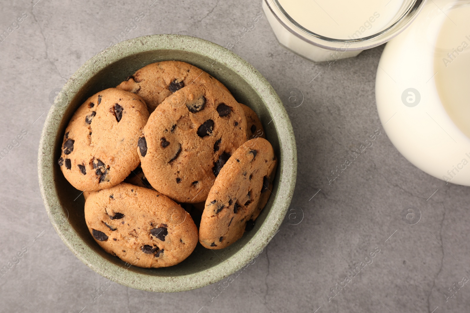 Photo of Delicious chocolate chip cookies and milk on grey table, flat lay