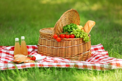 Photo of Wicker basket with food and juice on blanket in park. Summer picnic