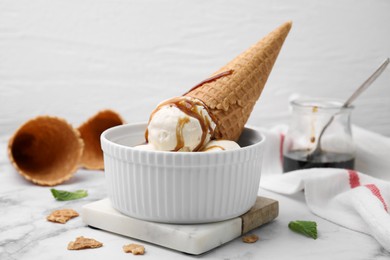 Photo of Scoopsice cream with caramel sauce and wafer cone on white marble table, closeup
