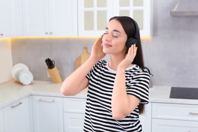Photo of Beautiful woman in headphones enjoying music in kitchen