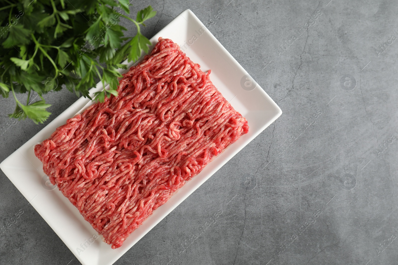 Photo of Raw ground meat and parsley on grey table, top view. Space for text