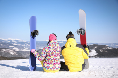 Young couple with snowboards on hill, back view. Winter vacation