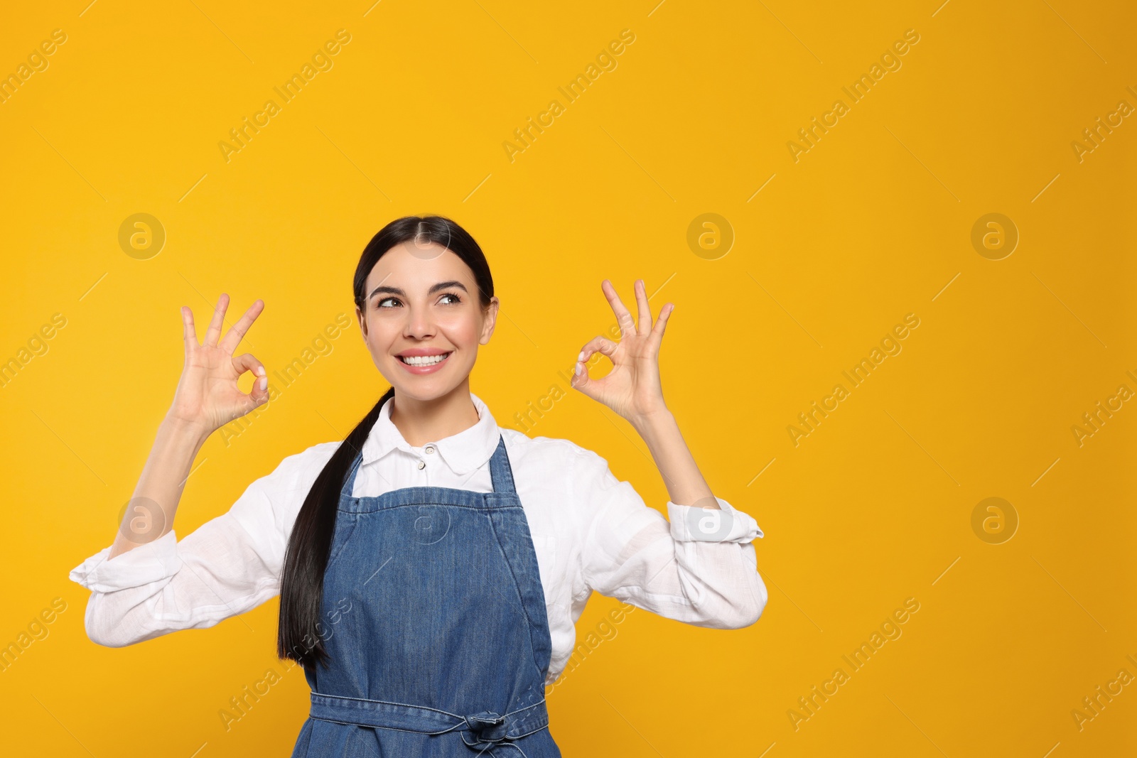 Photo of Young woman in blue jeans apron on yellow background, space for text