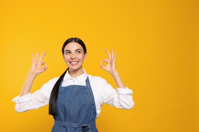 Young woman in blue jeans apron on yellow background, space for text